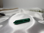 Treasured Energies polished malachite crystal tower with deep green banding resting on white satin fabric.