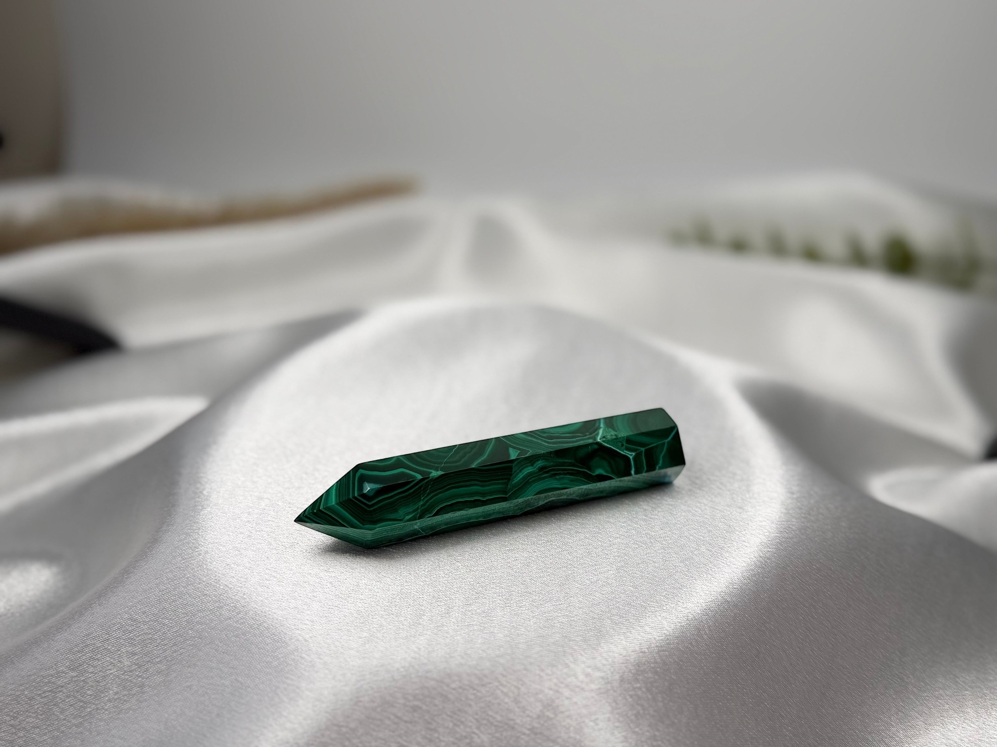 Treasured Energies polished malachite crystal tower with deep green banding resting on white satin fabric.