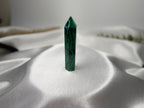 Treasured Energies polished malachite crystal tower with deep green banding on a soft white satin background.