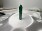 Treasured Energies polished malachite crystal tower with deep green banding on a soft white satin background