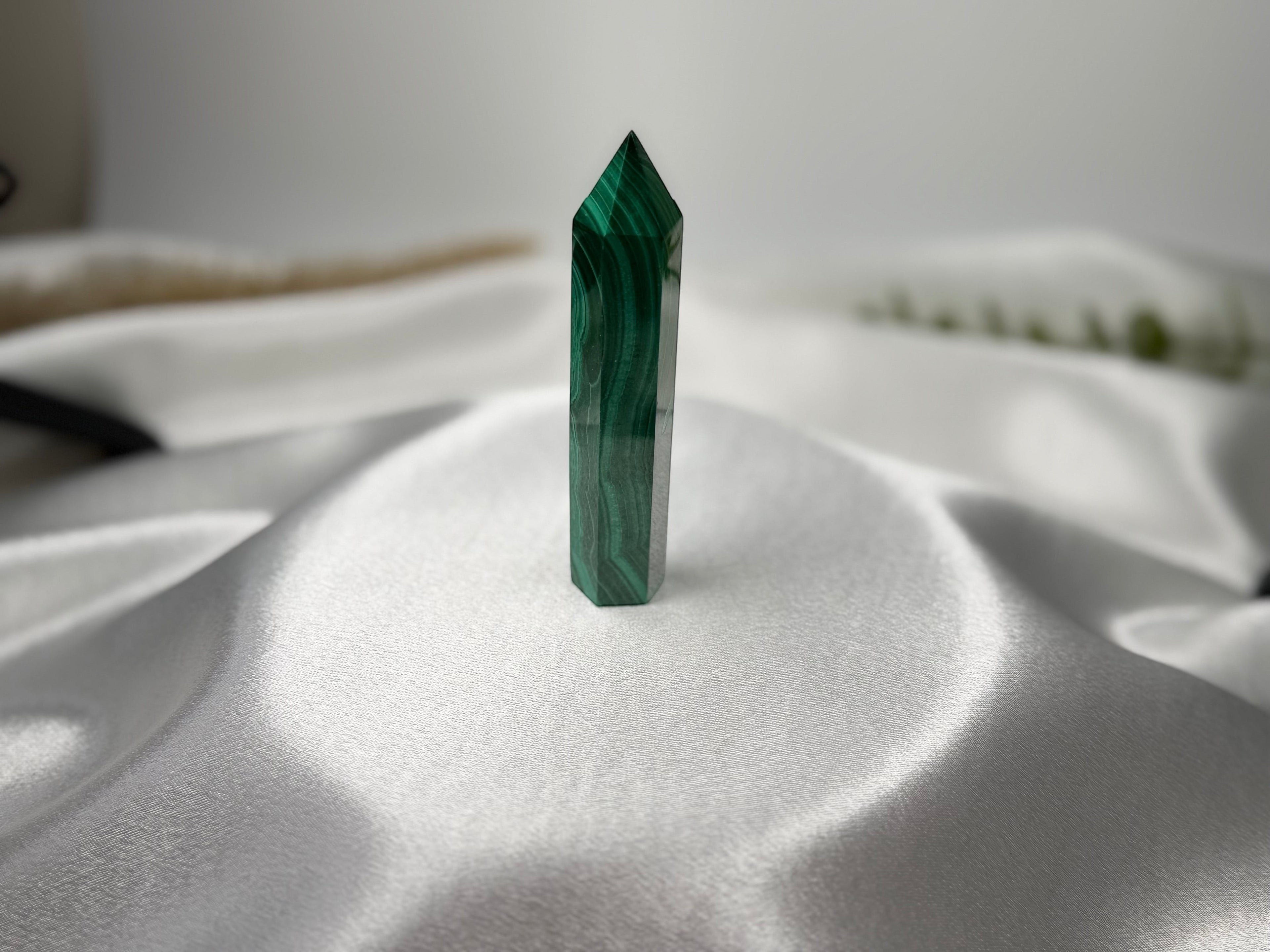Treasured Energies polished malachite crystal tower with deep green banding on a soft white satin background