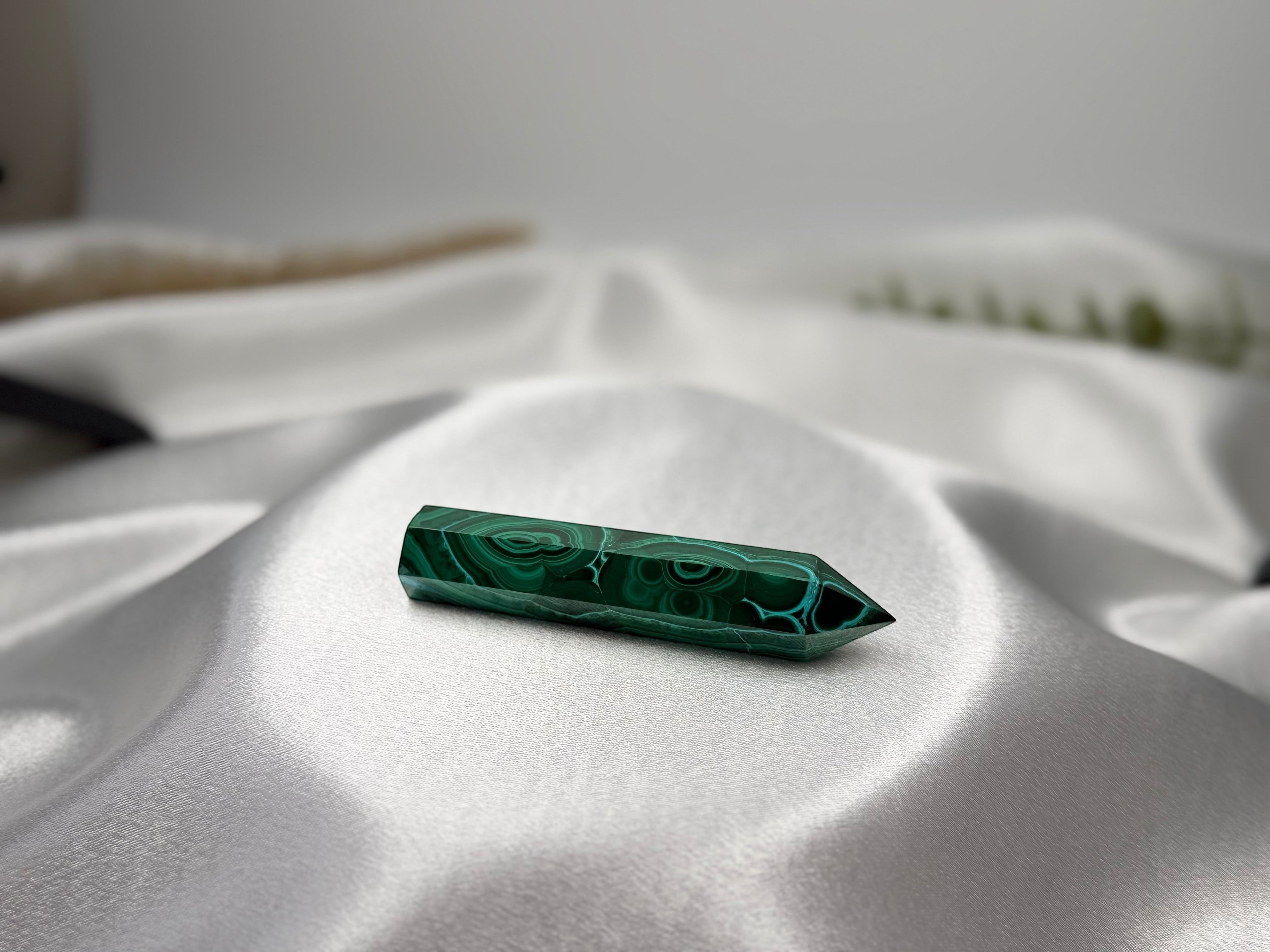 Treasured Energies polished malachite crystal generator tower with deep green banding on a white satin fabric background