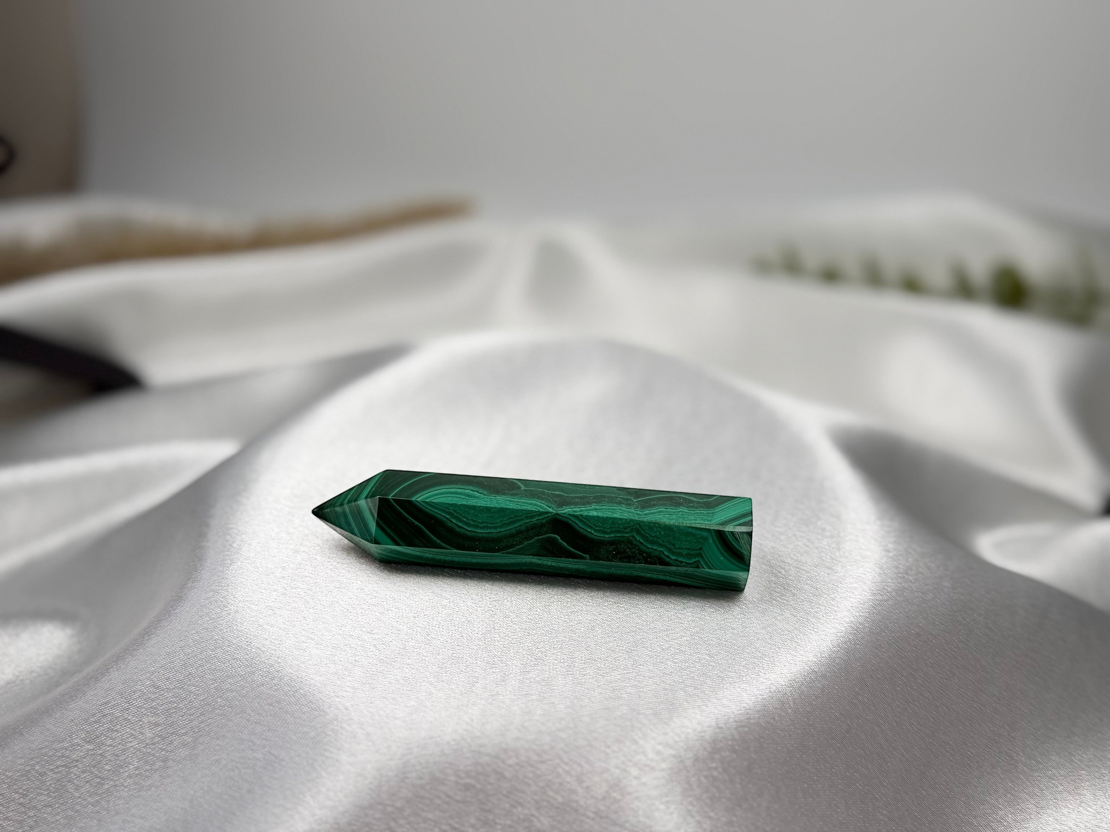 Treasured Energies polished malachite crystal generator tower with deep green banding on a soft white satin fabric.