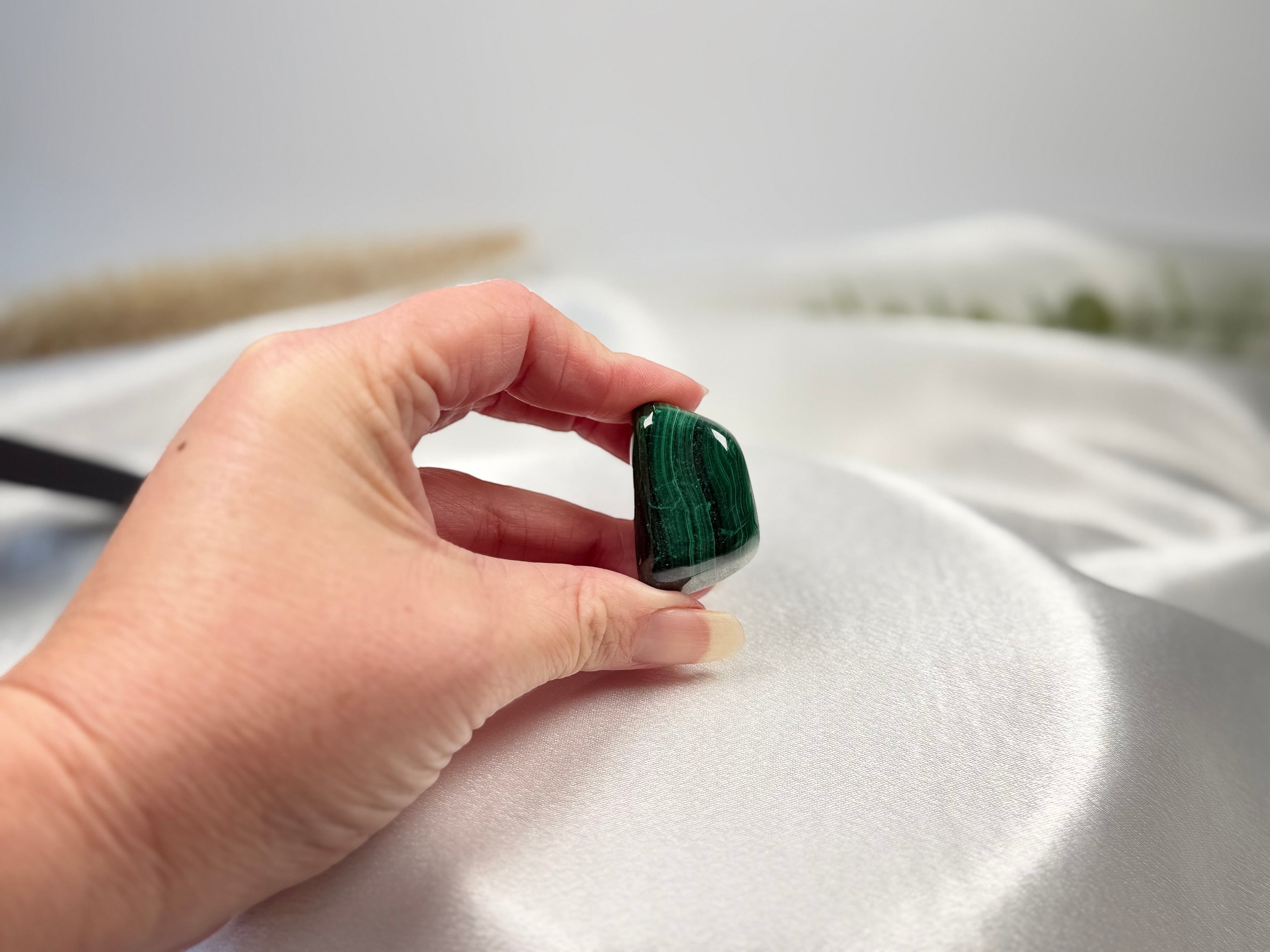 Treasured Energies high grade polished malachite tumbled stone with deep green banding held in a hand