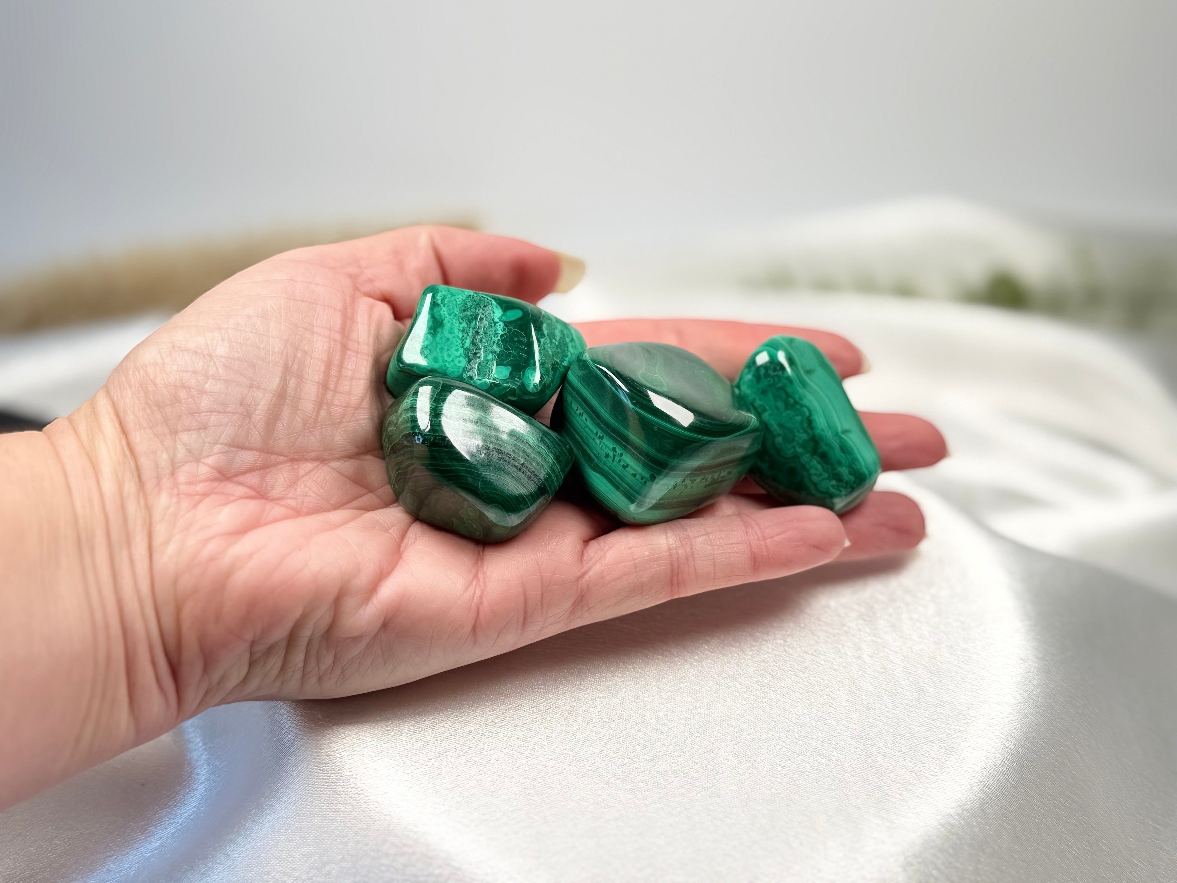Treasured Energies high grade polished malachite tumbled stones held in a hand showing vibrant green banded patterns