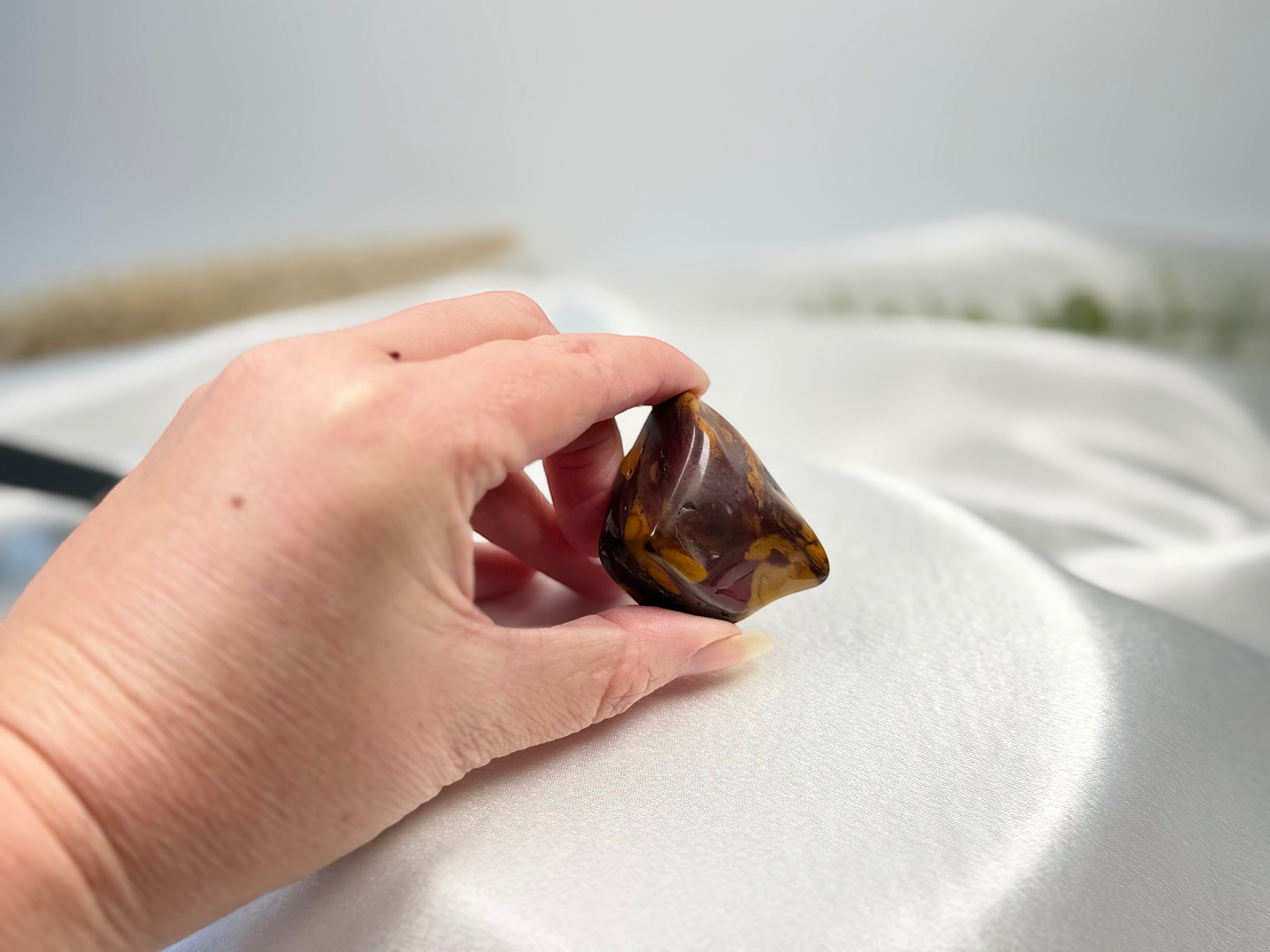 Treasured Energies large polished Mookaite jasper tumble stone with red, burgundy, and yellow tones held in a hand