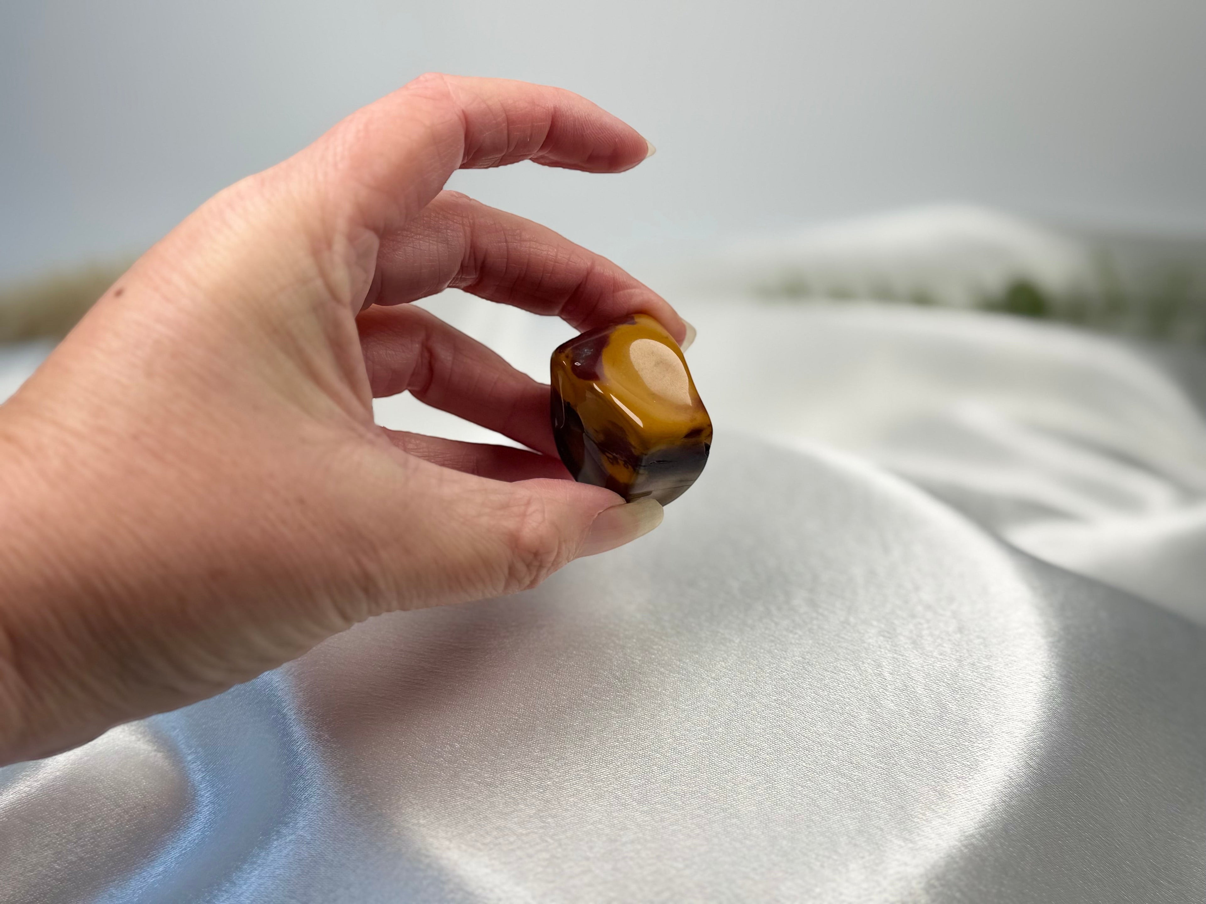 Treasured Energies large polished Mookaite jasper tumbled stone with red, burgundy, and yellow earthy tones in a hand.