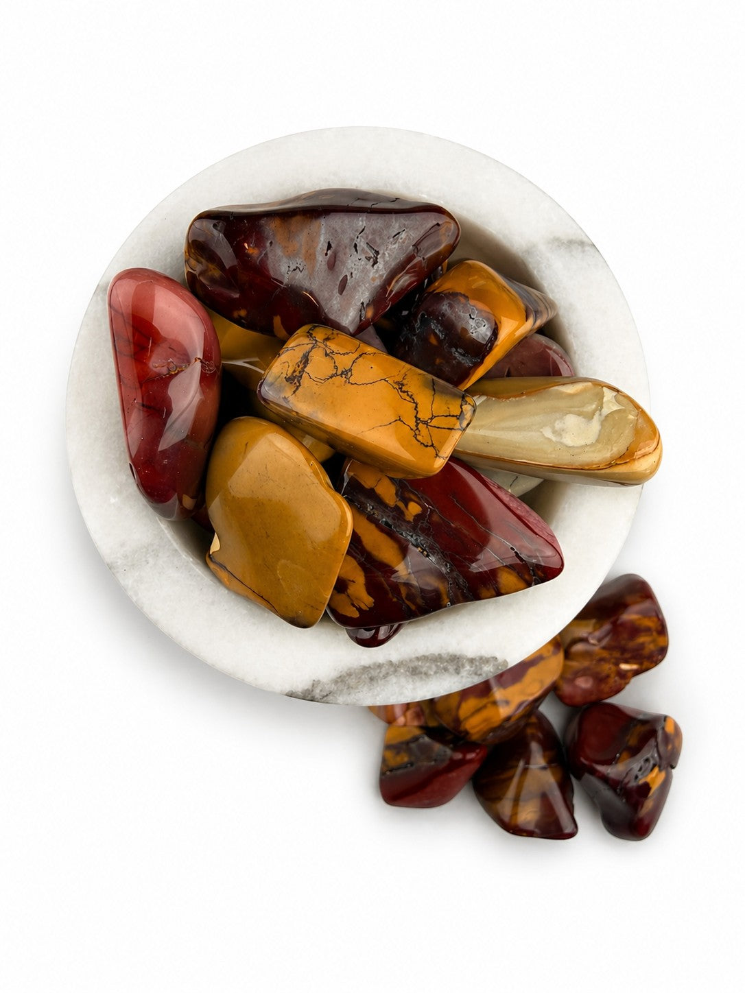 Treasured Energies high grade Mookaite tumbled stones in warm red, burgundy, and yellow tones inside a marble bowl.