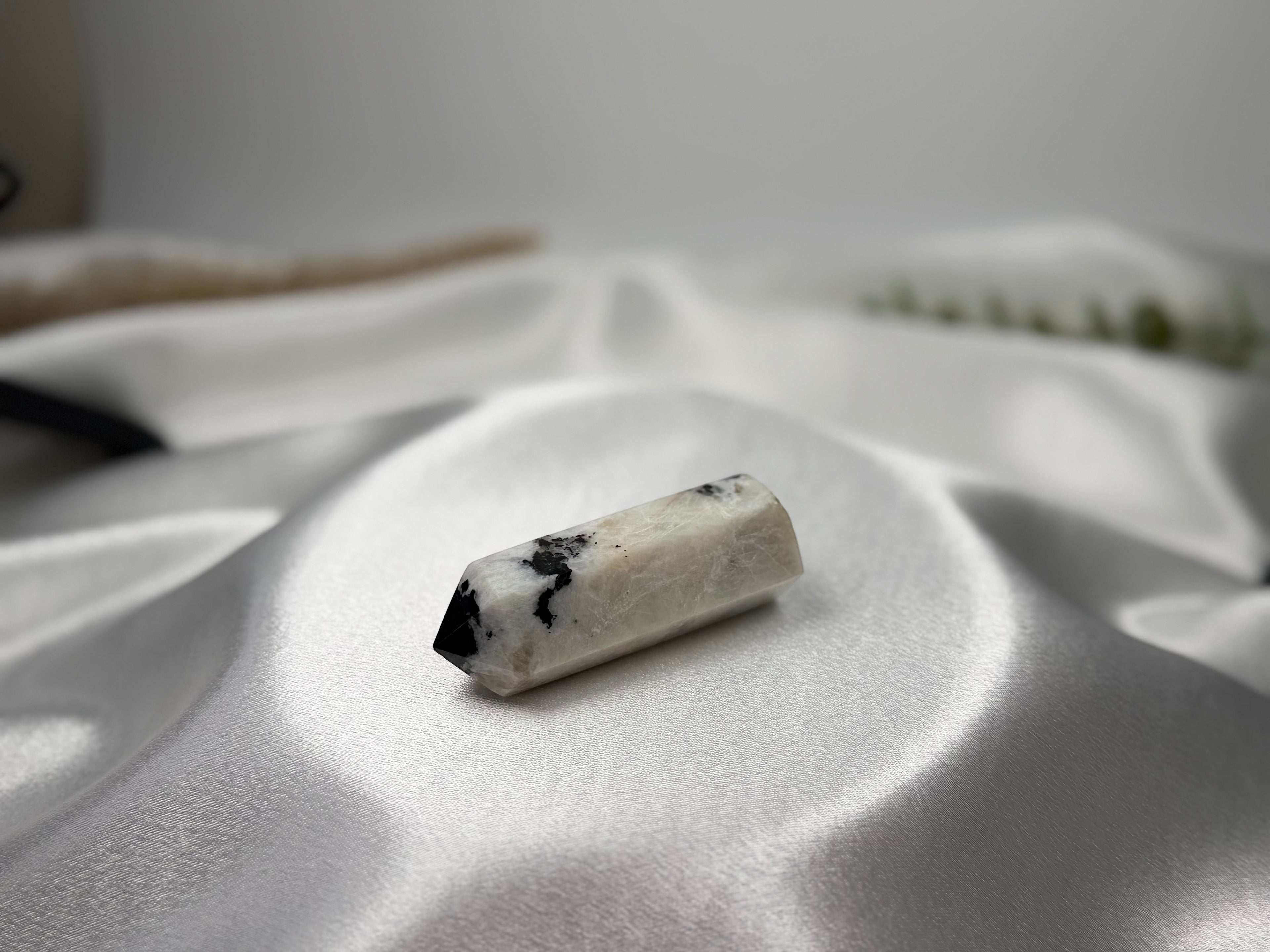 Treasured Energies moonstone crystal tower with white and black natural inclusions resting on a white silk fabric.