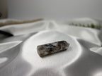 Treasured Energies moonstone crystal tower with grey and black inclusions resting on white satin fabric