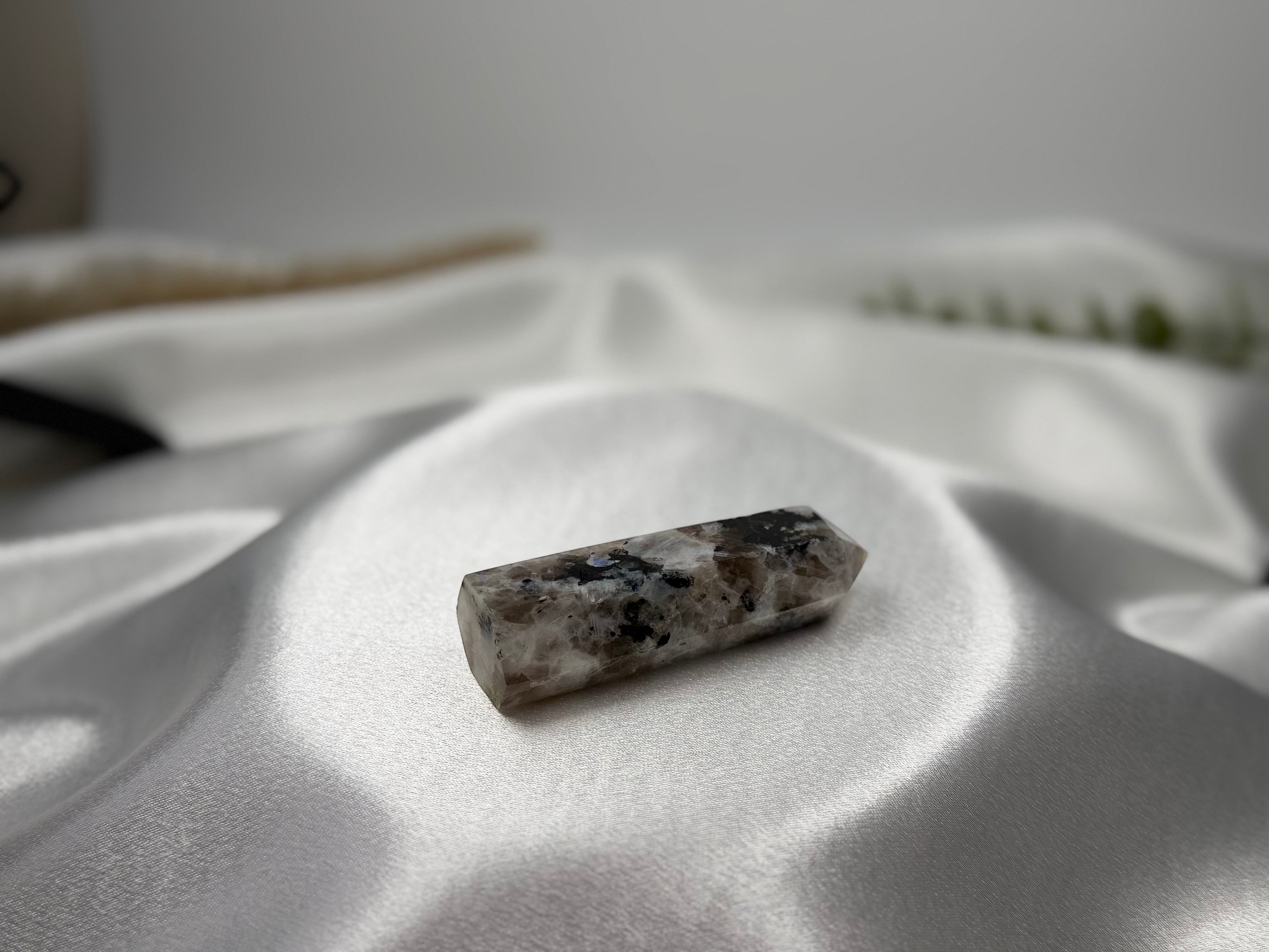 Treasured Energies moonstone crystal tower with grey and black inclusions resting on white satin fabric