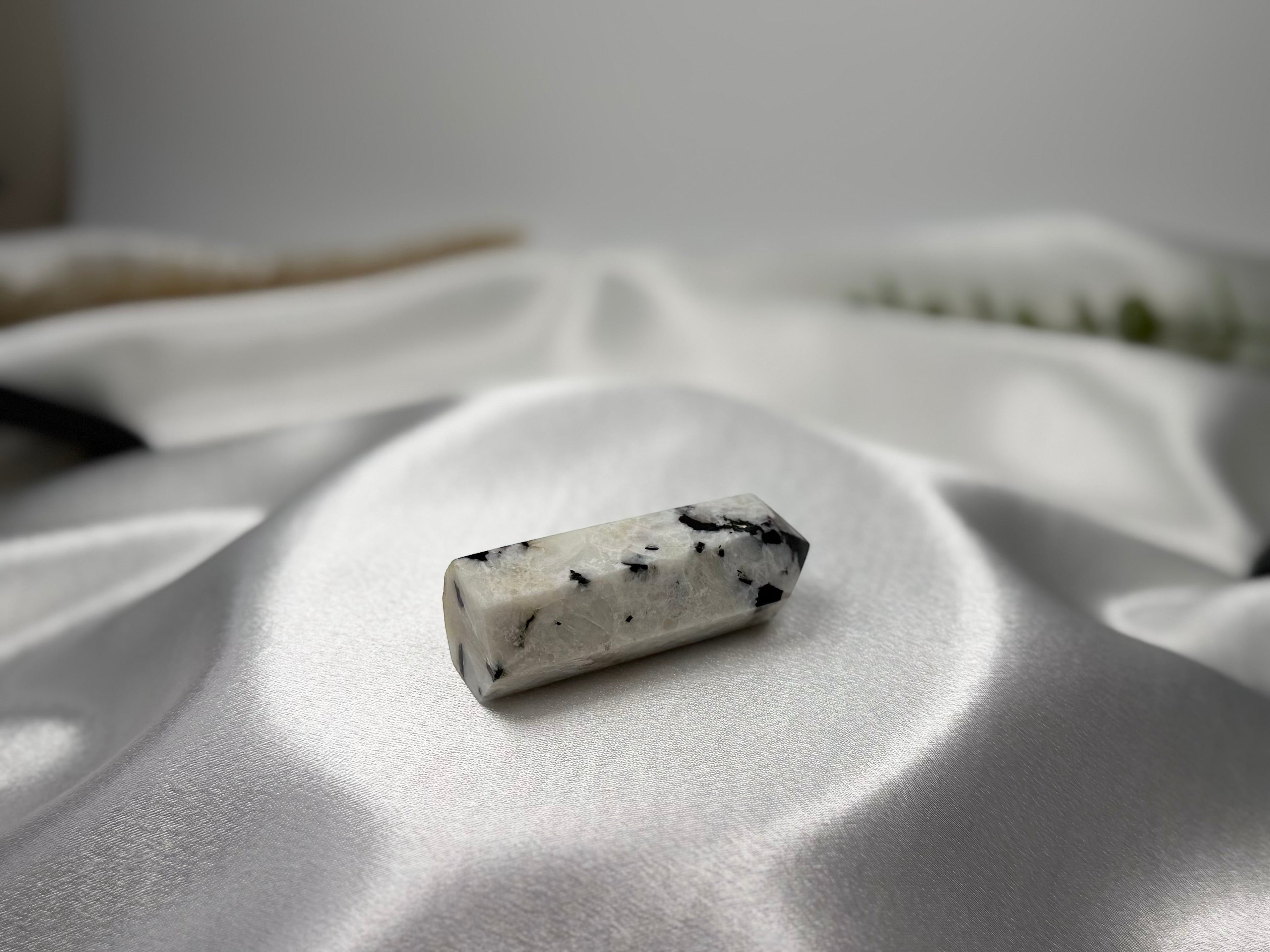 Treasured Energies moonstone crystal tower with black inclusions resting on a white satin fabric background.