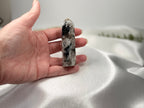 Treasured Energies moonstone crystal tower held in a hand, featuring white and black mineral inclusions.