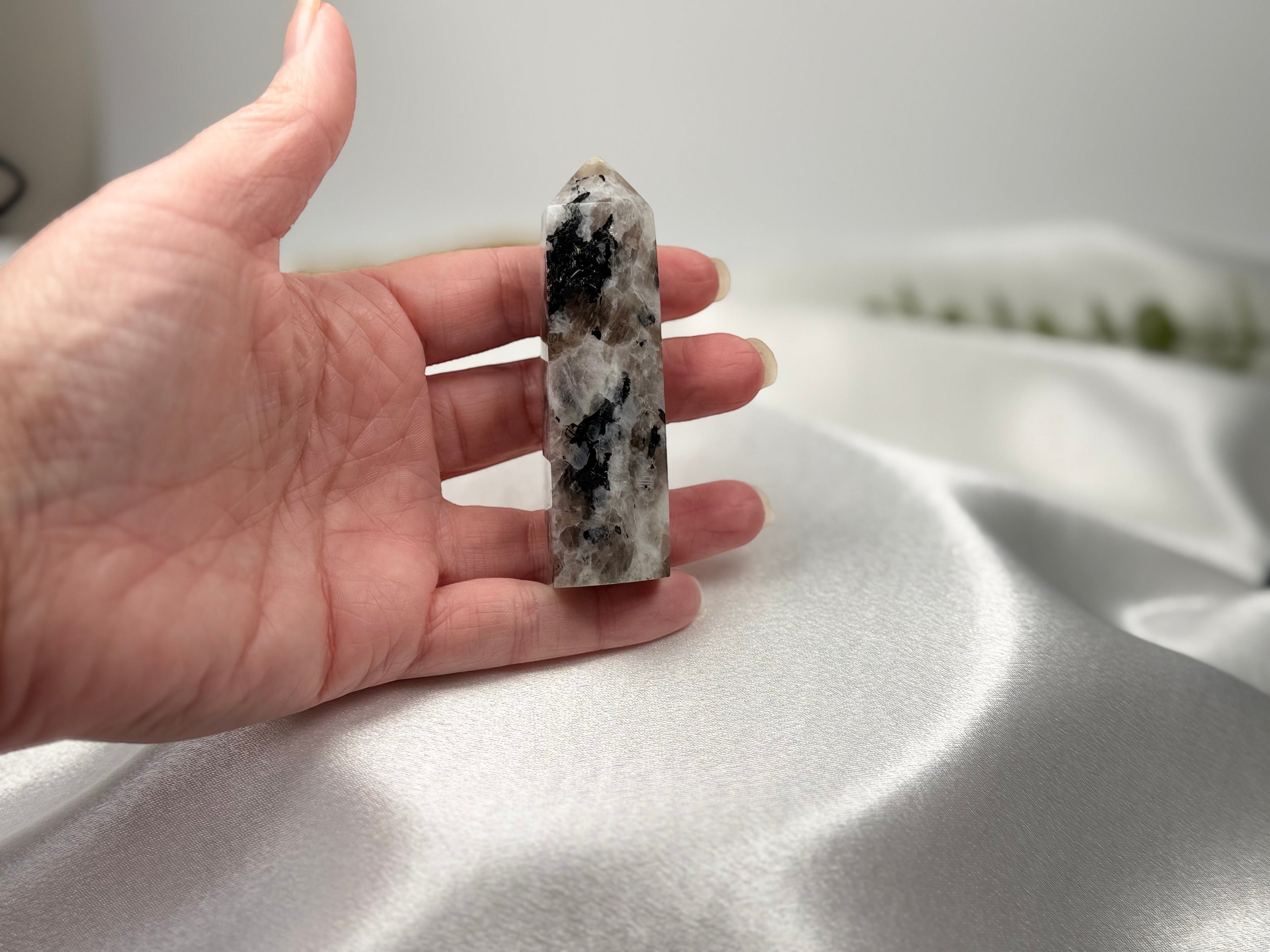 Treasured Energies moonstone crystal tower held in a hand, featuring white and black mineral inclusions.
