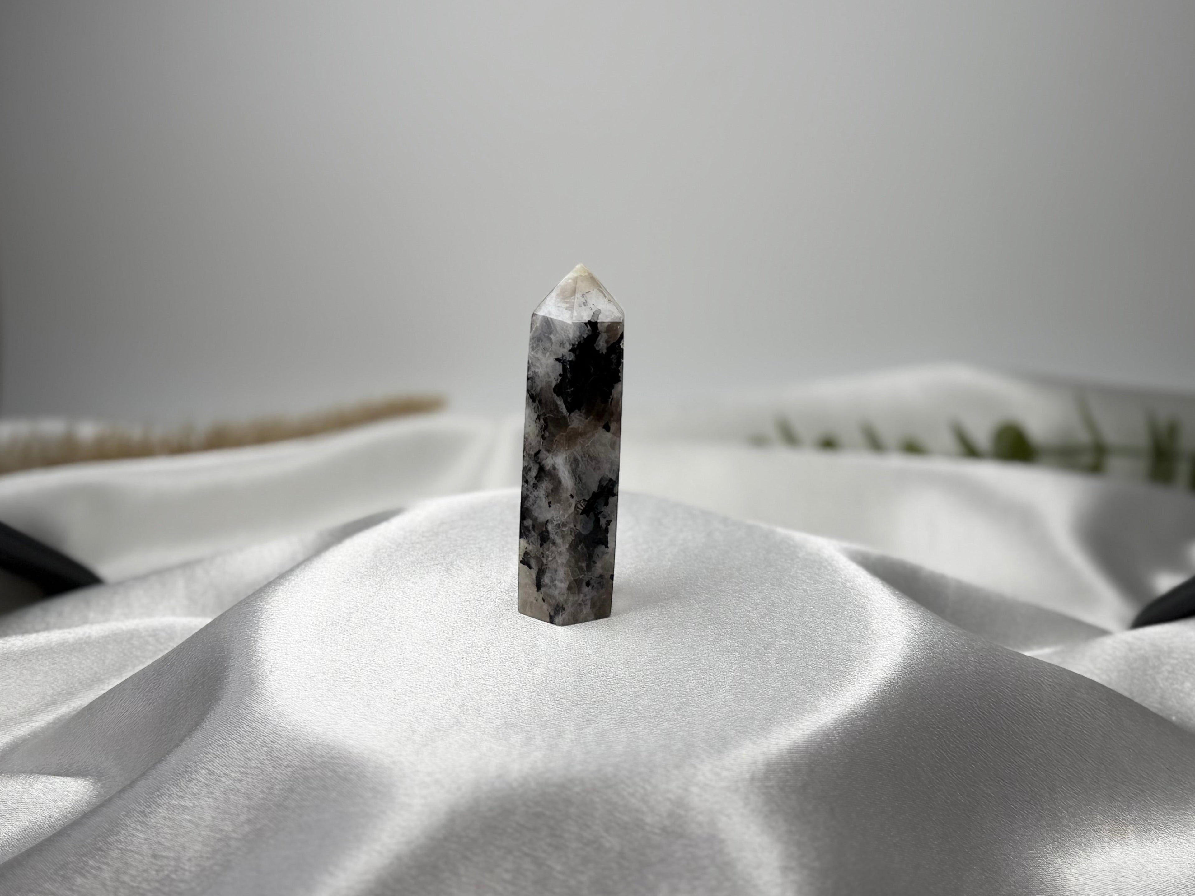 Treasured Energies moonstone crystal tower with black and white patterns standing on a draped white satin fabric.