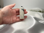 Treasured Energies moonstone crystal tower held in a hand, featuring milky white stone with black mineral inclusions.