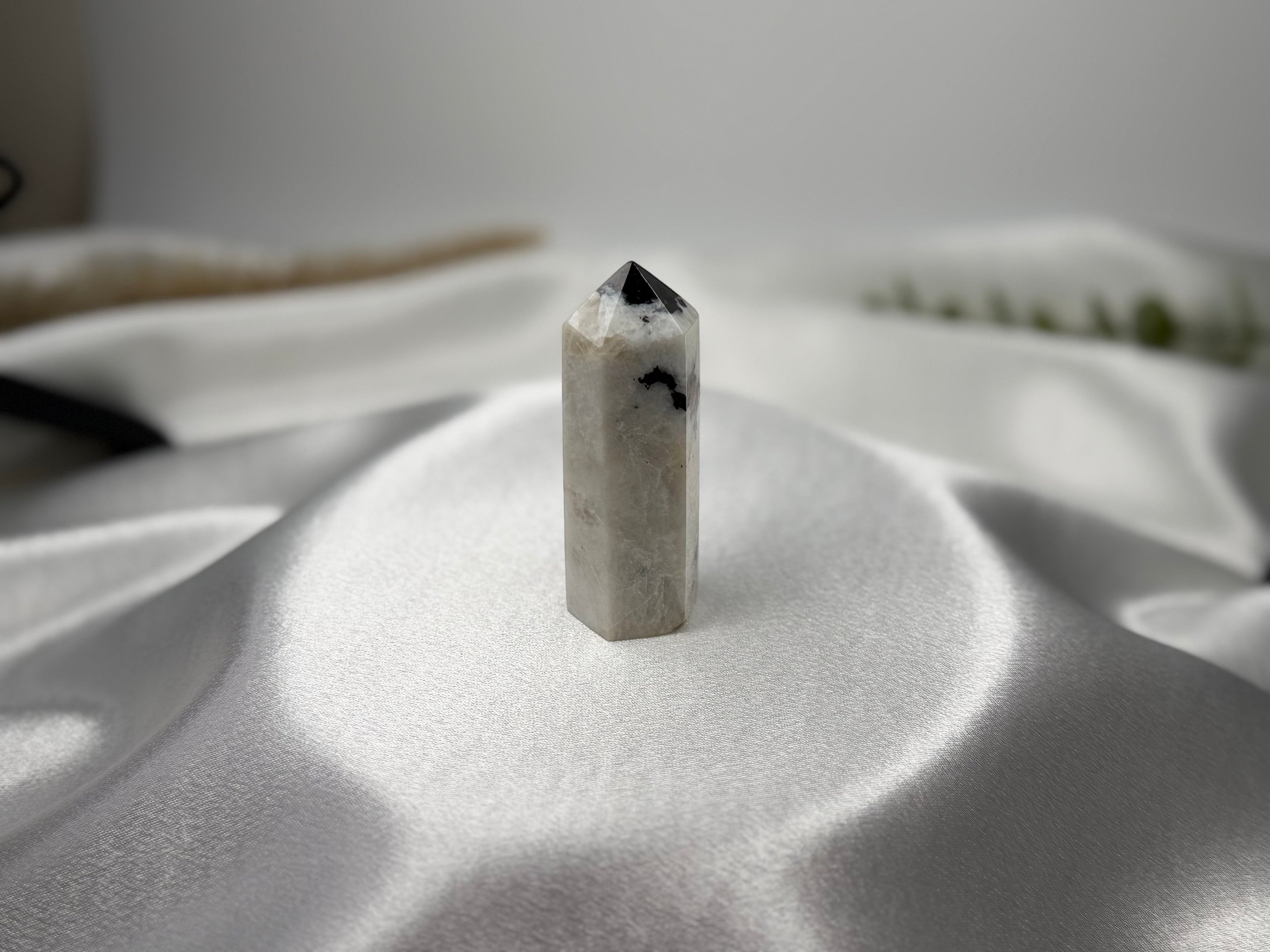 Treasured Energies moonstone crystal tower with black inclusions on a white satin background