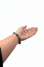 Treasured Energies moss agate crystal bead bracelet worn on a wrist while holding a small decorative hedgehog figurine