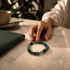 Treasured Energies moss agate crystal bead bracelet on a marble table next to a journal and coffee cup