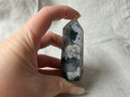 Treasured Energies polished Moss Agate crystal tower held in hand, showing green moss-like inclusions and grey quartz.