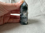 Treasured Energies polished Moss Agate crystal tower with green moss-like inclusions held against a linen background.
