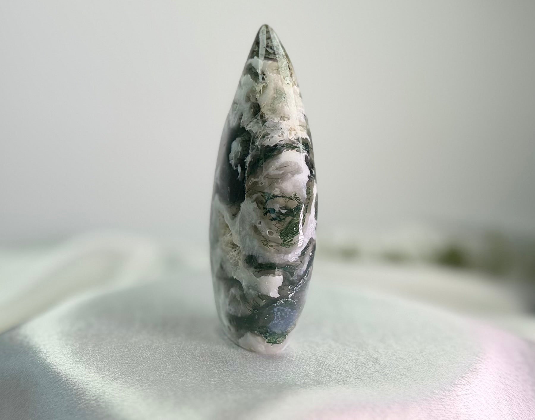 Treasured Energies polished moss agate flame crystal sculpture with green and white mineral patterns on a white cloth.