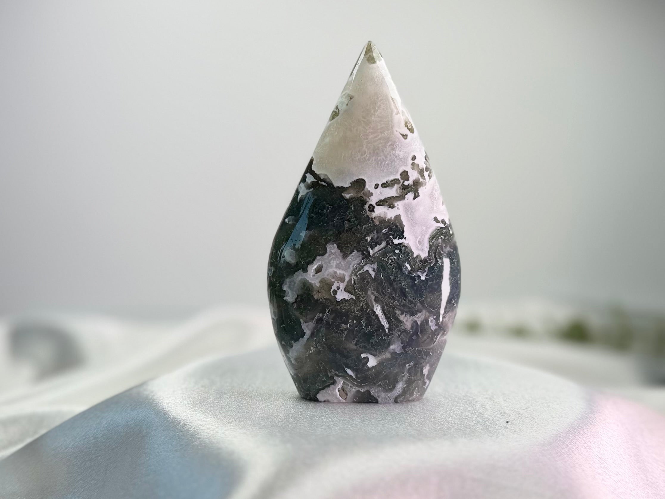 Treasured Energies polished Moss Agate freeform crystal with green and white earthy inclusions on a white surface.