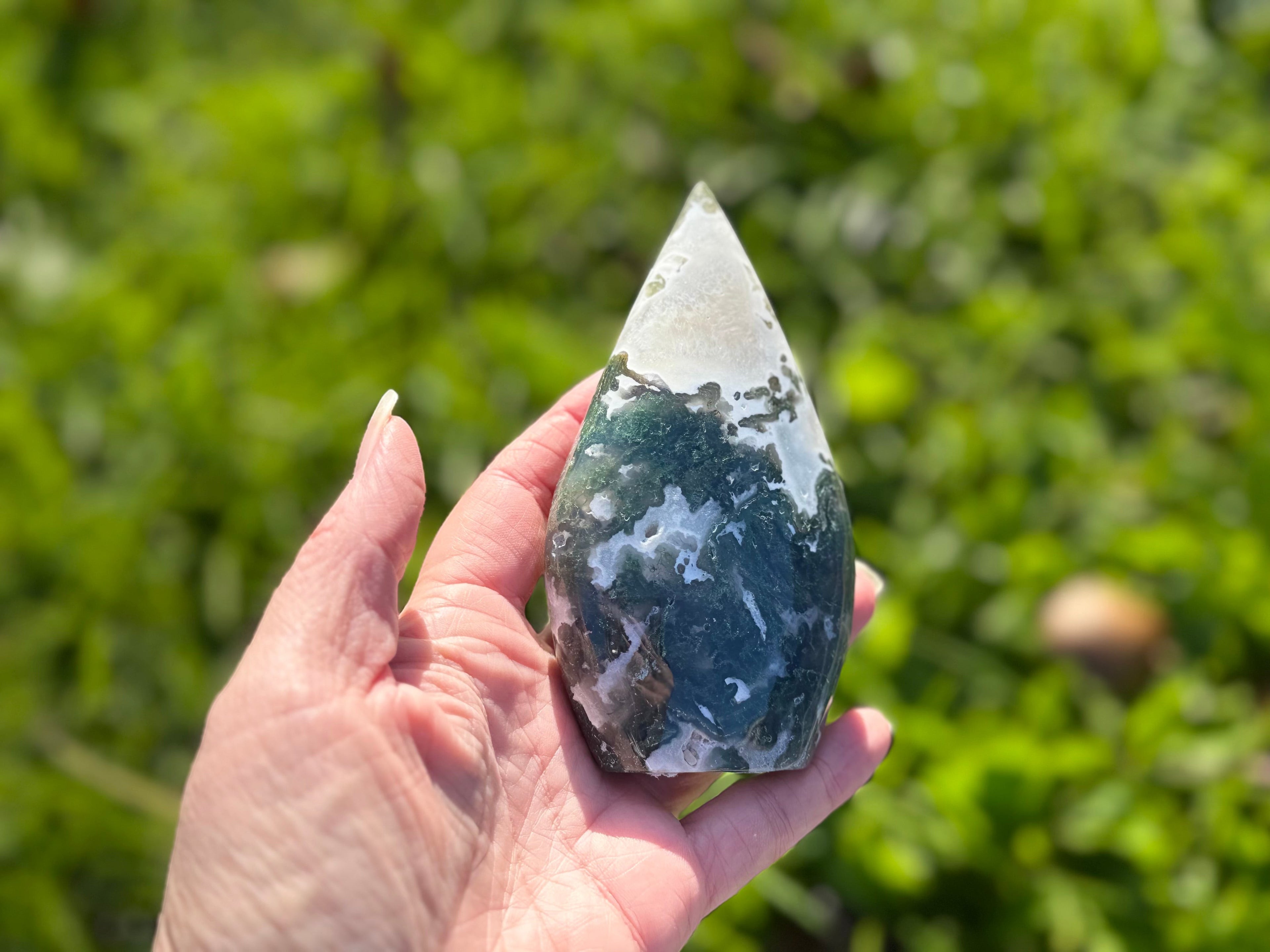 Treasured Energies hand-polished moss agate freeform crystal with green mossy inclusions held in a palm outdoors.