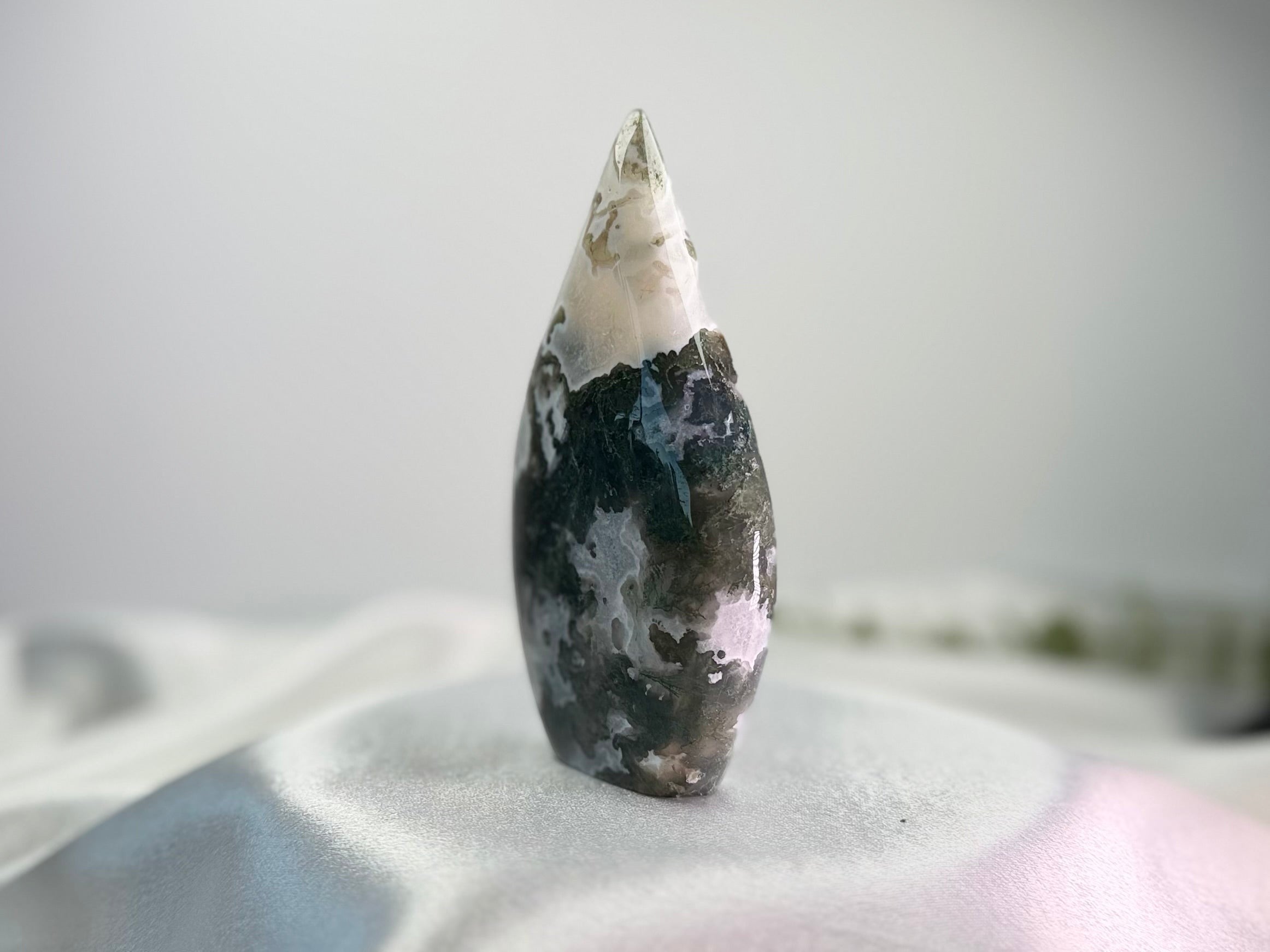 Treasured Energies polished Moss Agate freeform crystal with green and white organic inclusions on a white fabric base.