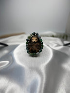 Treasured Energies moss agate crystal bead bracelet encircling a small brown hedgehog figurine on white satin fabric