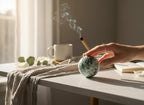 Treasured Energies polished moss agate crystal sphere held by a hand on a desk with incense smoke and a coffee mug.