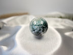 Treasured Energies polished moss agate crystal sphere with green and white earthy inclusions on a white satin cloth.
