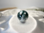 Treasured Energies polished moss agate crystal sphere with deep green moss-like inclusions on a white satin cloth.