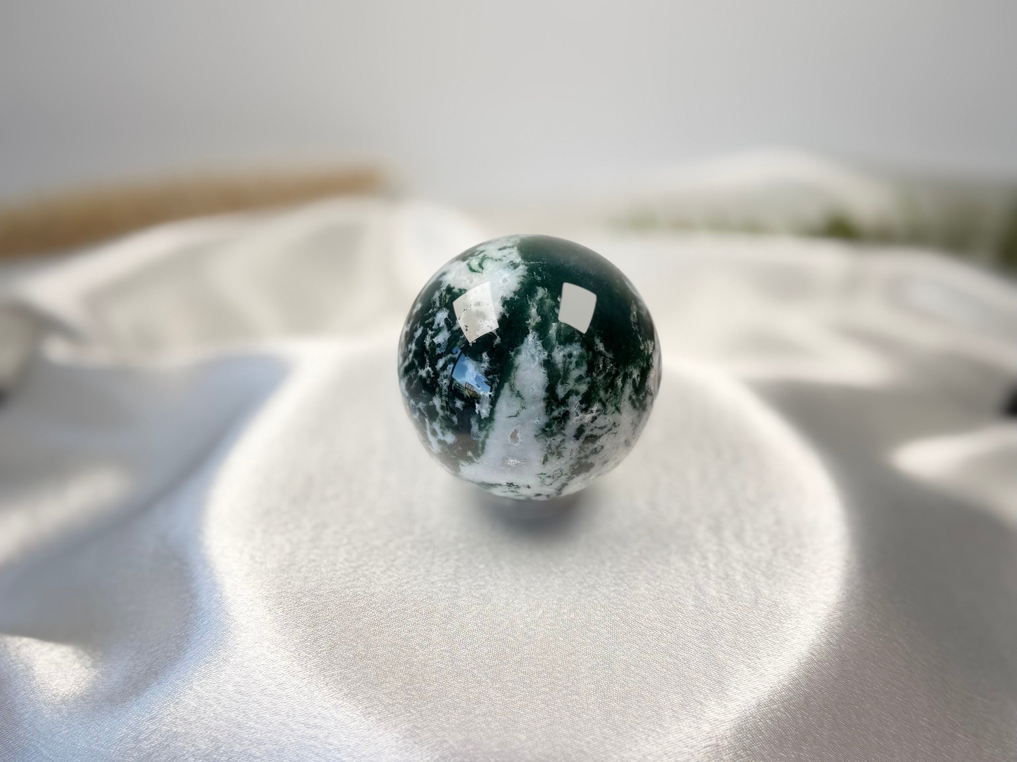 Treasured Energies polished moss agate crystal sphere with deep green moss-like inclusions on a white satin cloth.