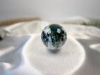 Treasured Energies polished moss agate crystal sphere with deep green moss-like inclusions on a white satin fabric
