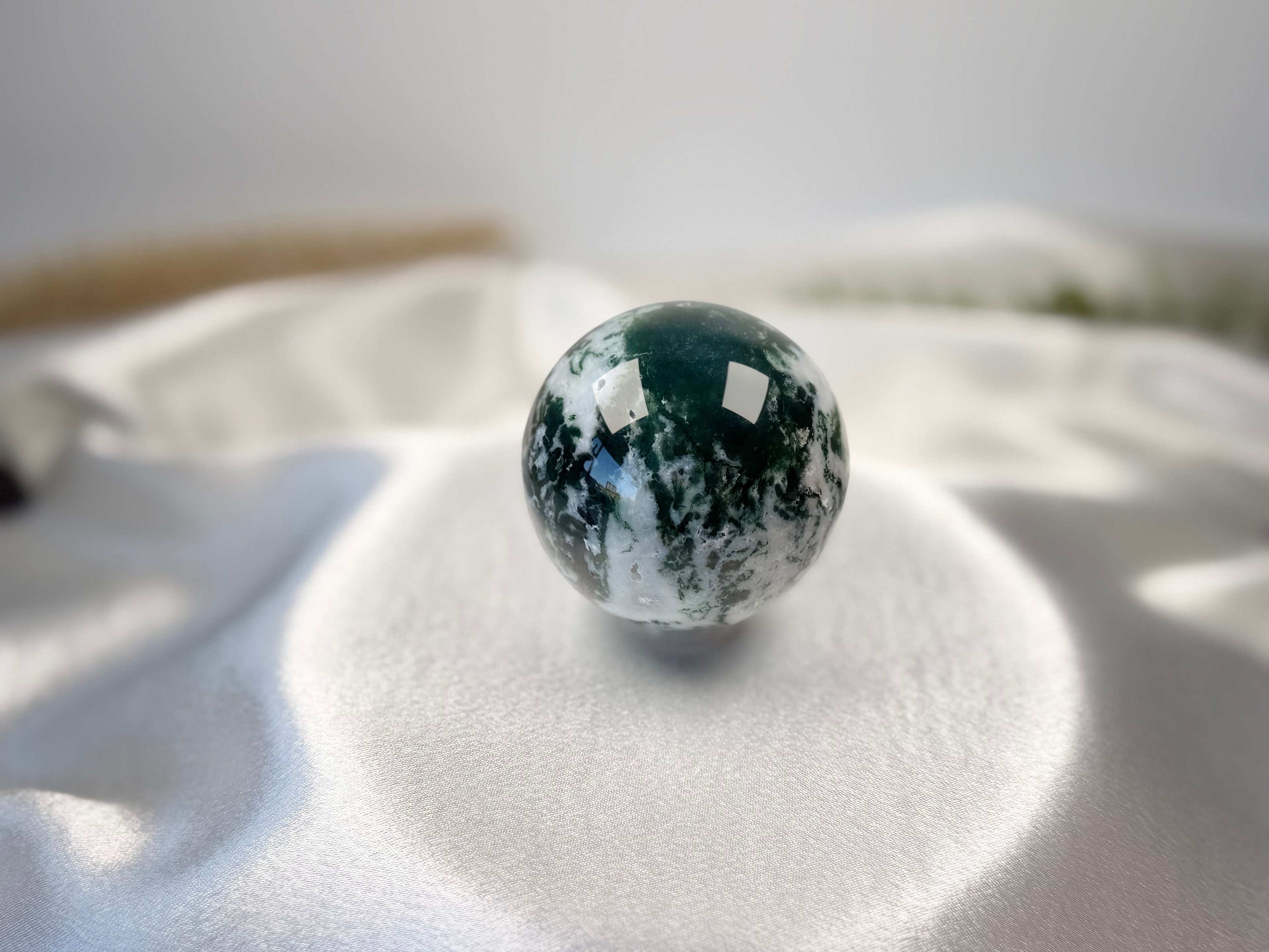 Treasured Energies polished moss agate crystal sphere with deep green moss-like inclusions on a white satin fabric