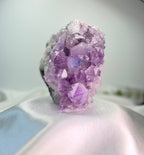 Treasured Energies natural amethyst crystal cluster with deep purple pointed points on a soft white satin background.
