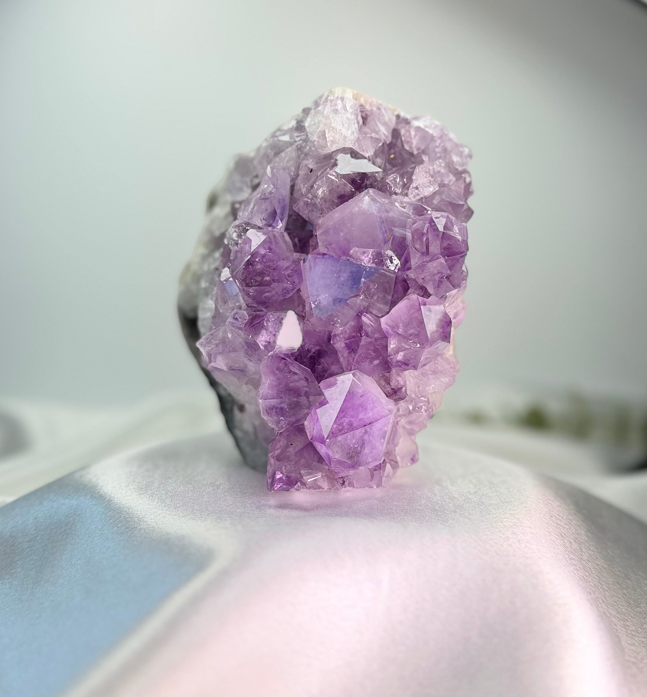 Treasured Energies natural amethyst crystal cluster with deep purple pointed points on a soft white satin background.