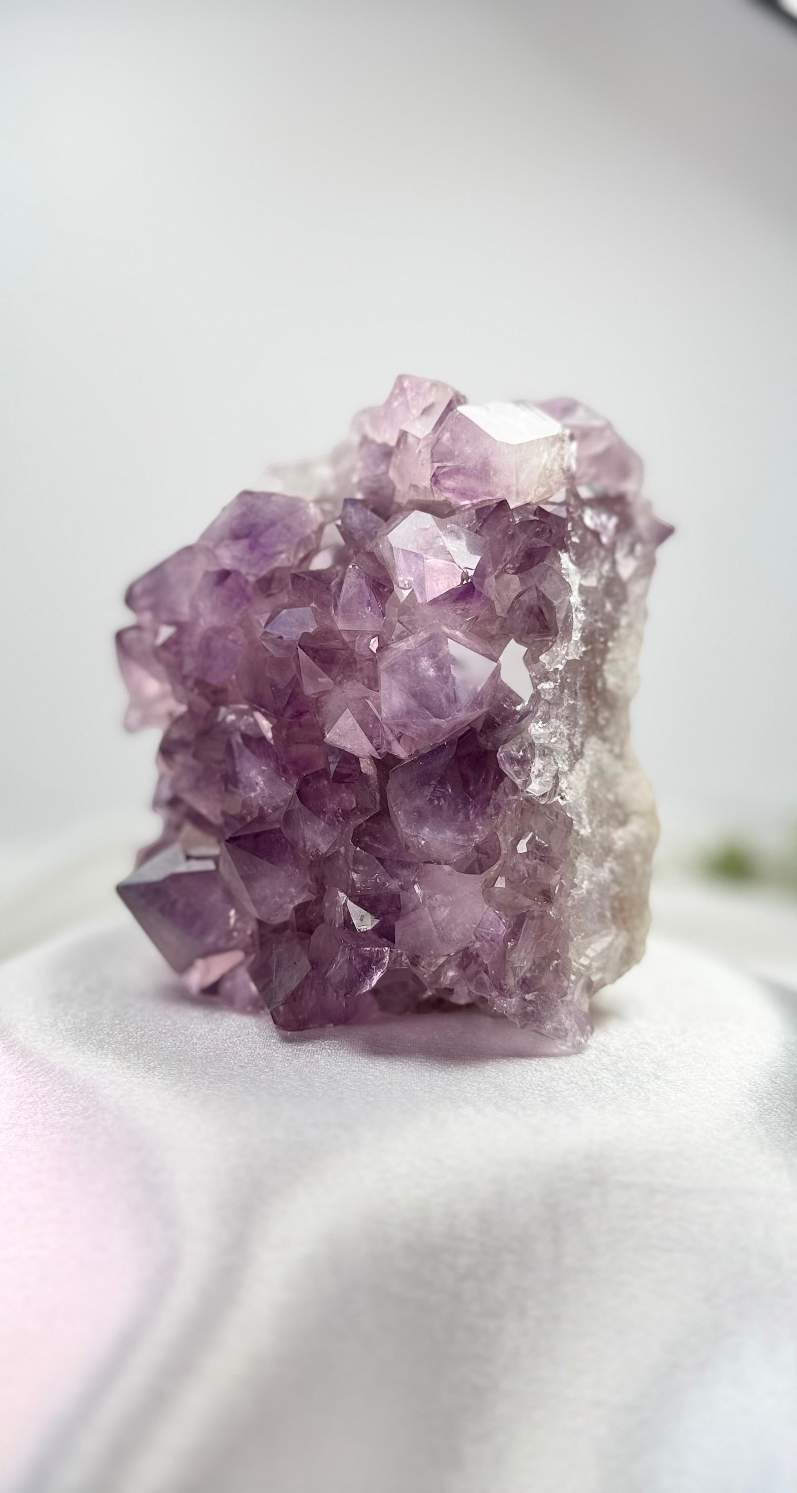 Treasured Energies natural amethyst crystal cluster with deep purple pointed points on a white satin surface.