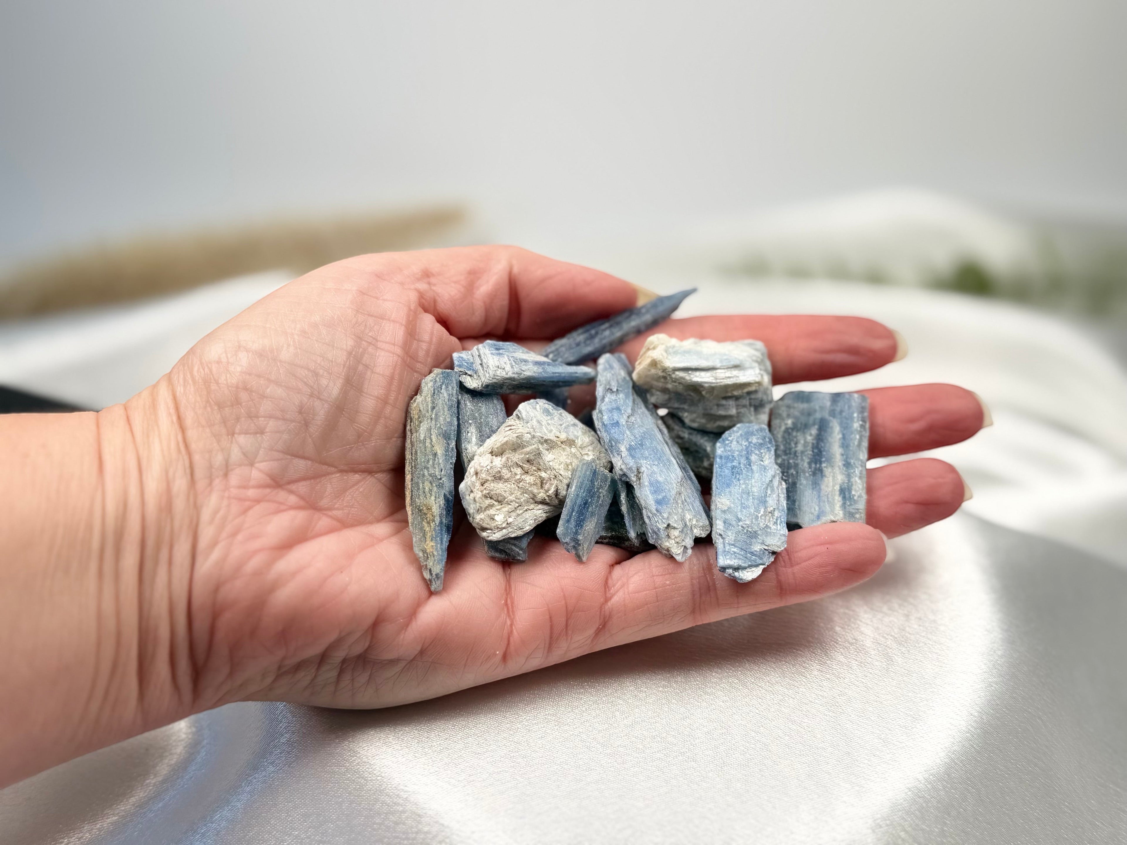 Treasured Energies natural blue kyanite crystal stones held in a palm against a soft white fabric background.