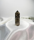 Treasured Energies dark brown and grey Ocean Jasper crystal tower with circular orb patterns on a white satin cloth