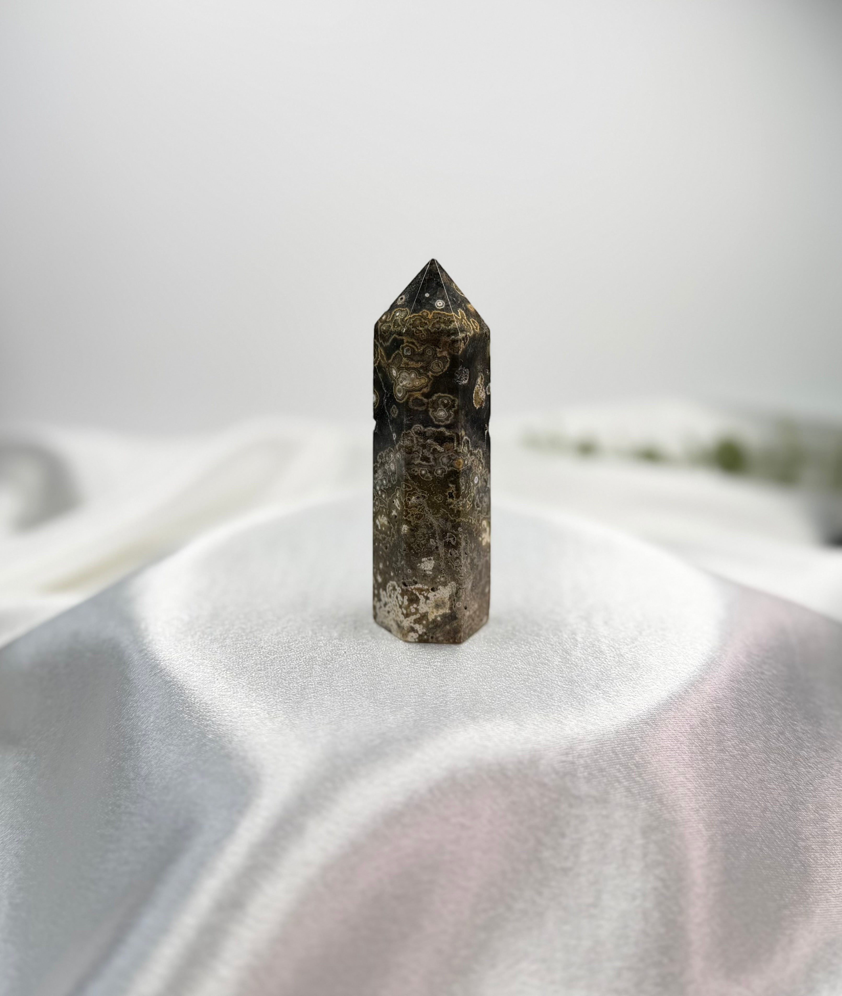 Treasured Energies dark brown and grey Ocean Jasper crystal tower with circular orb patterns on a white satin cloth