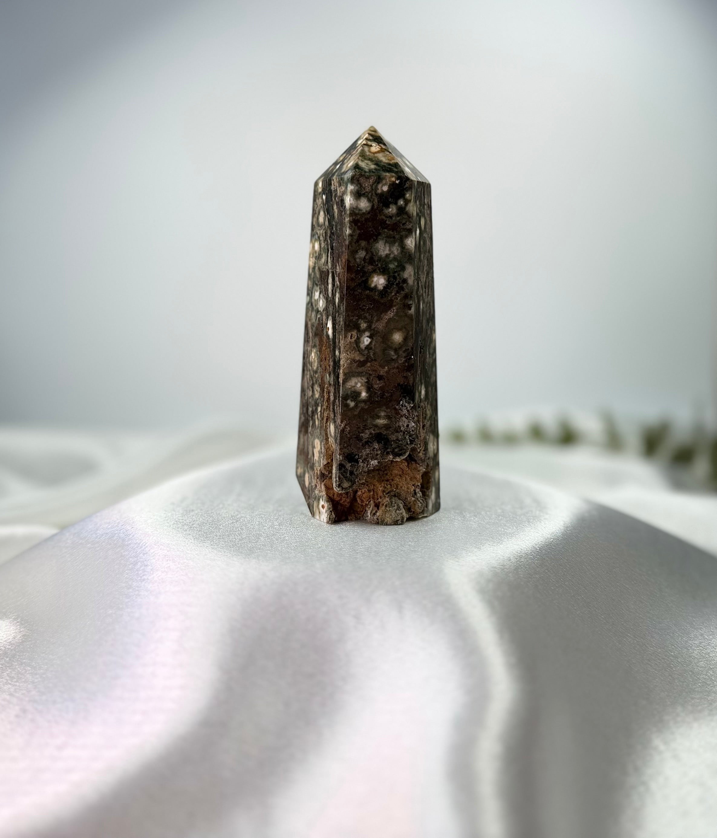 Treasured Energies polished Ocean Jasper crystal tower with natural orbicular patterns on a white satin background