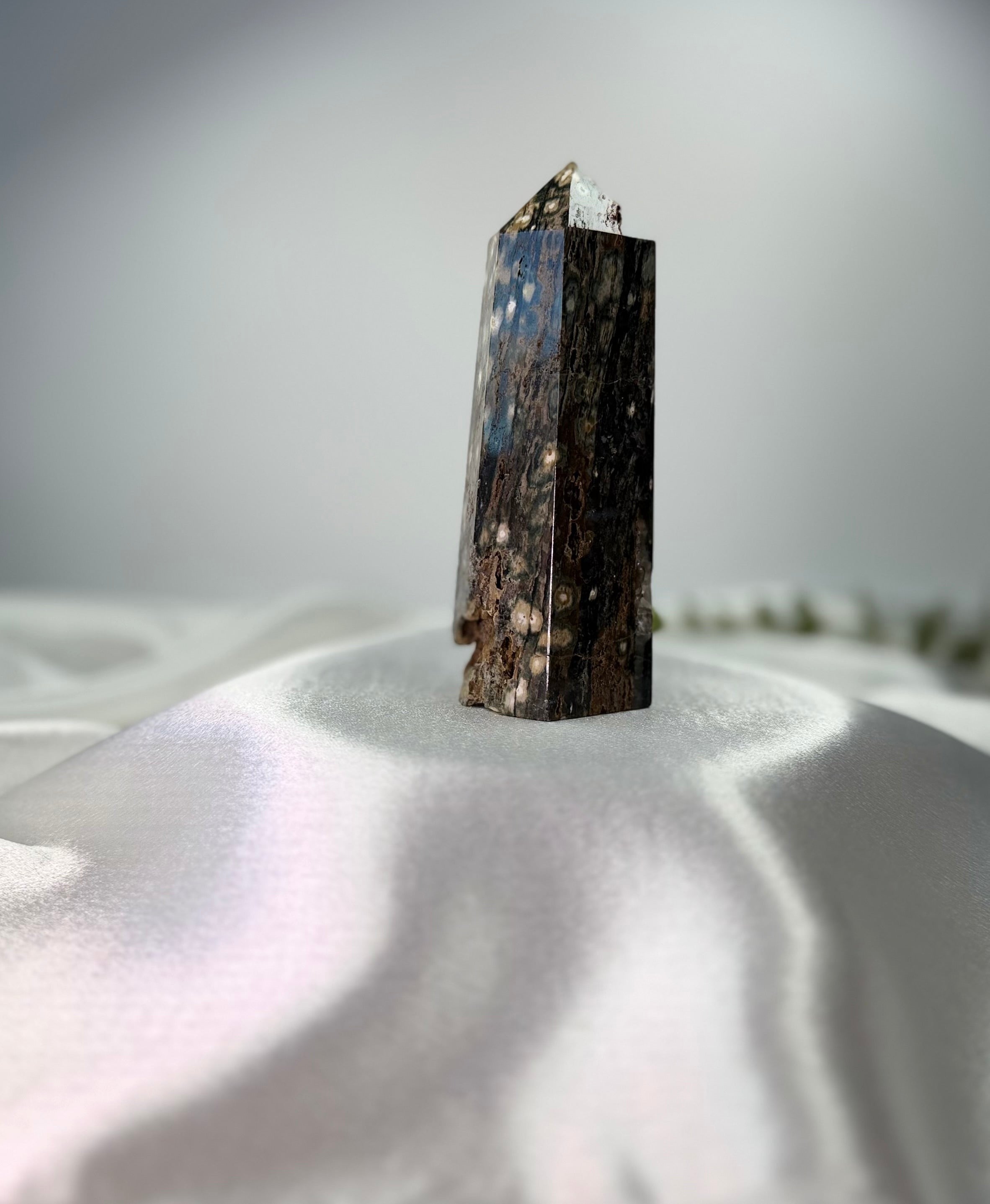 Treasured Energies polished Ocean Jasper crystal tower with dark brown tones and orbicular patterns on white silk.
