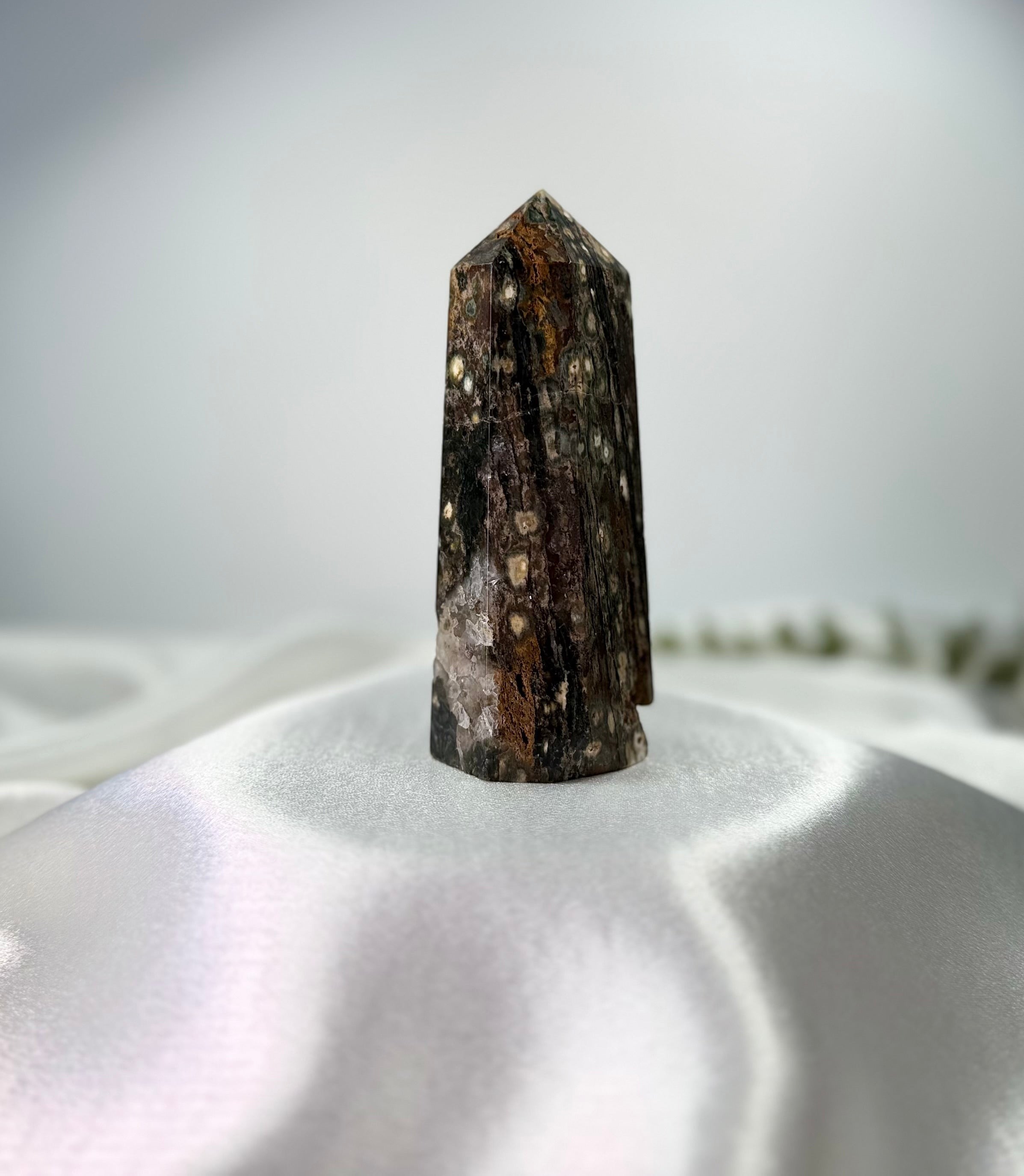 Treasured Energies polished Ocean Jasper crystal tower with dark brown and cream orbicular patterns on white silk.