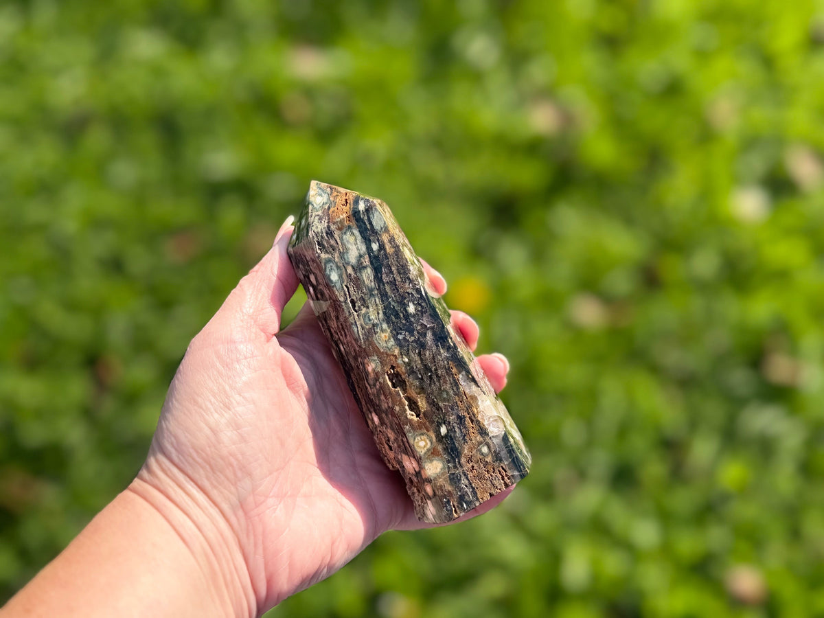 Treasured Energies polished Ocean Jasper crystal tower held in hand against a blurred green outdoor background