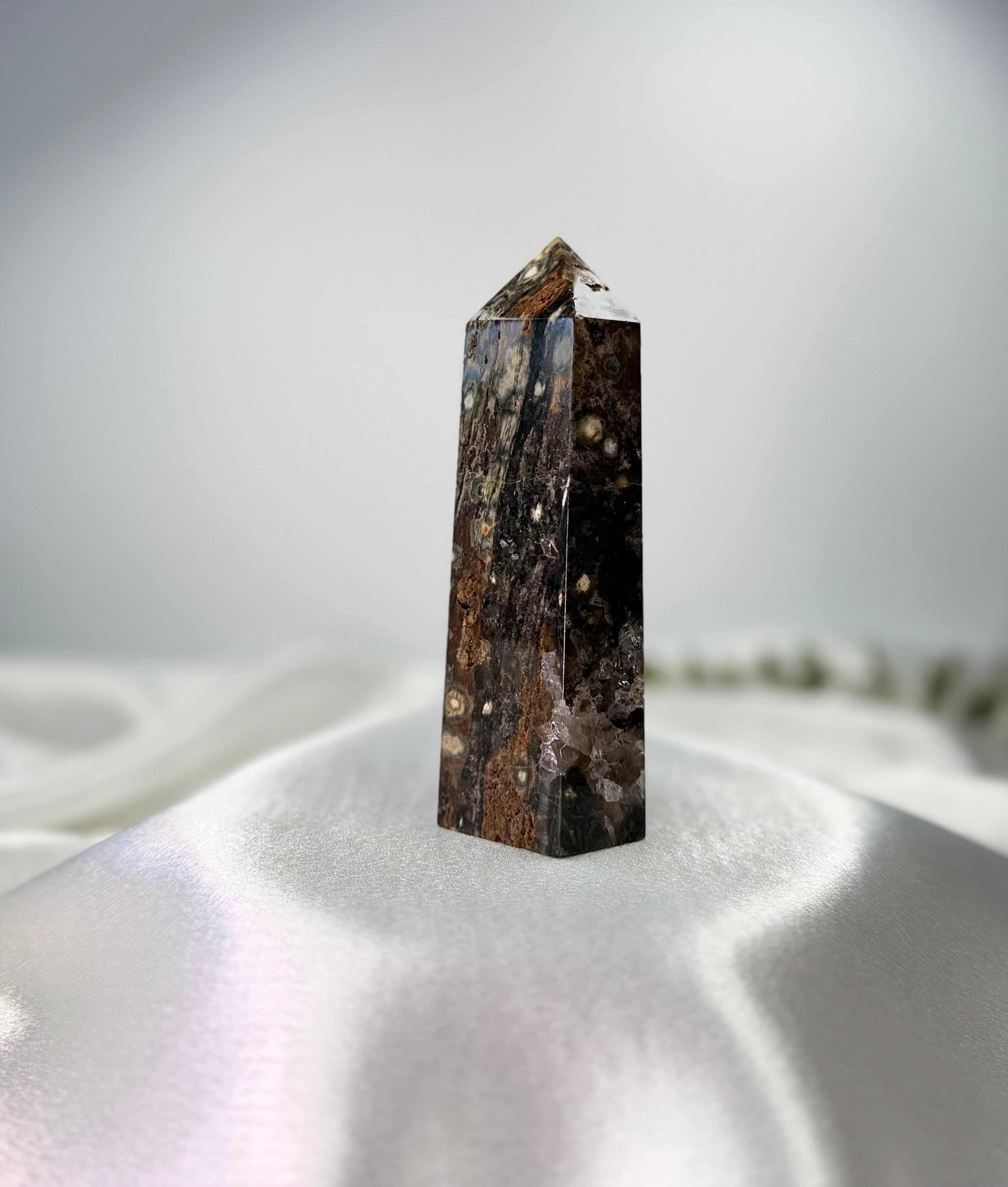 Treasured Energies polished Ocean Jasper crystal tower with dark brown and cream orbicular patterns on white silk.