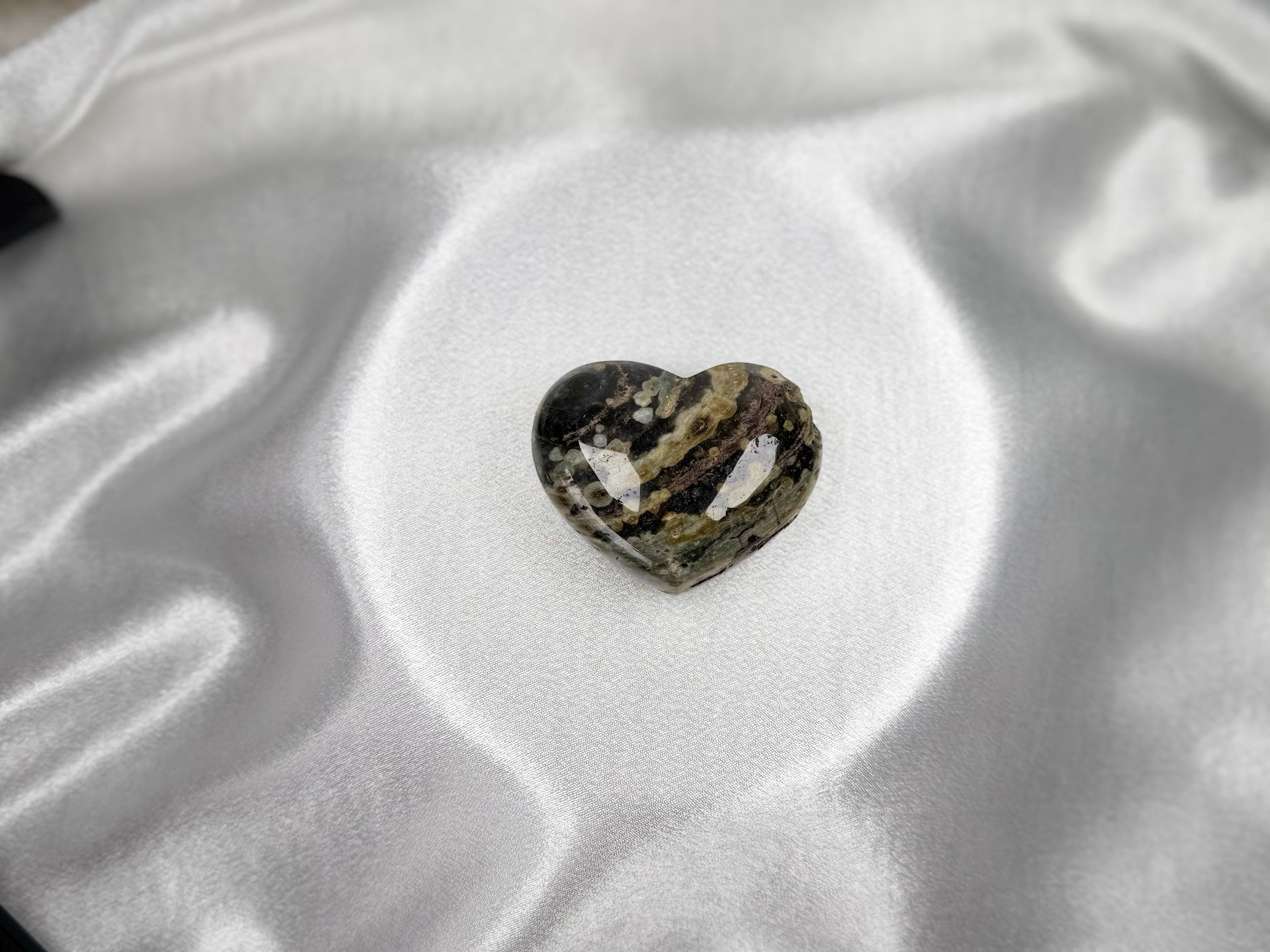 Treasured Energies large heart-shaped Ocean Jasper crystal with rhythmic green, brown, and black patterns on silk.