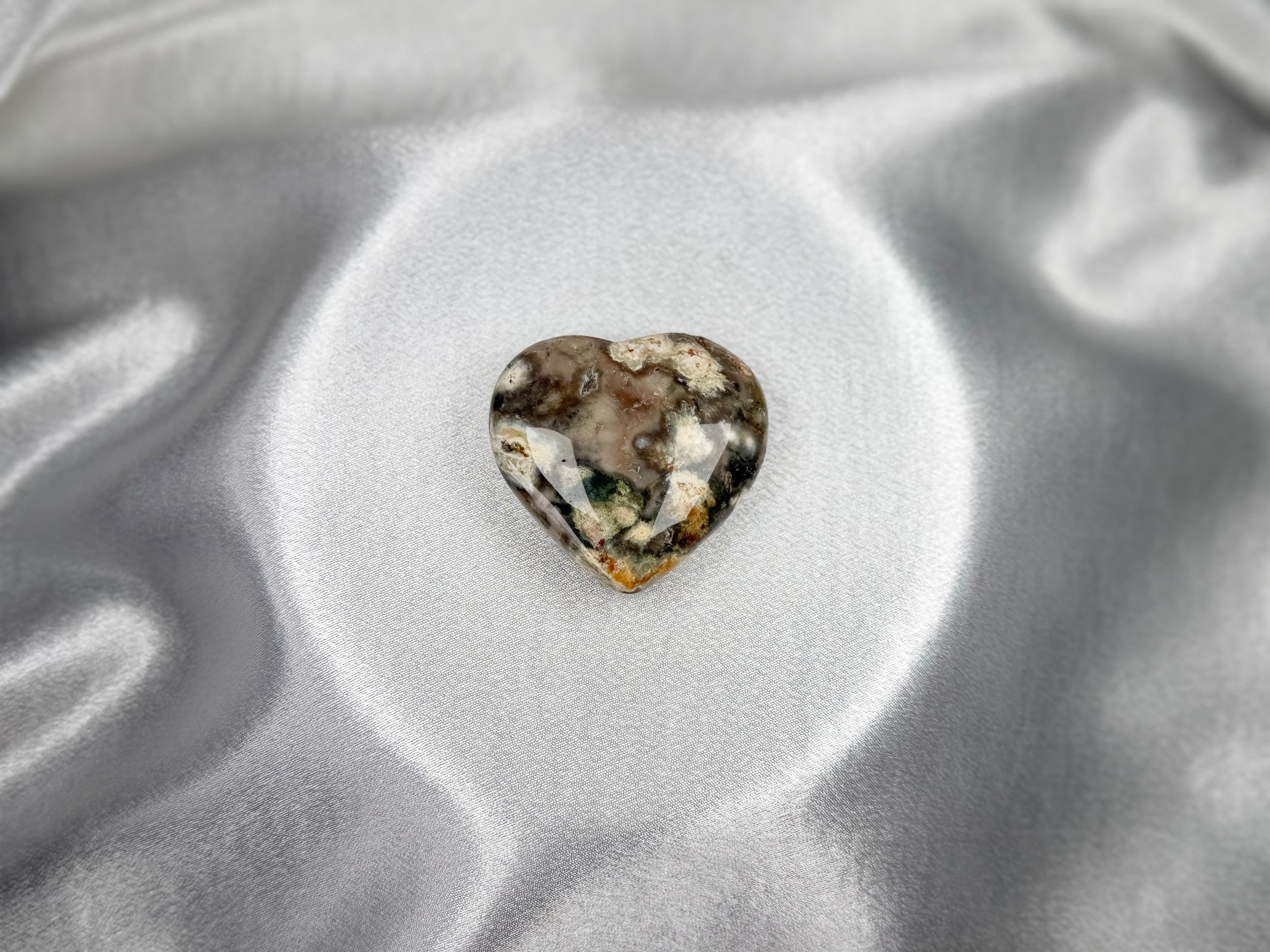 Treasured Energies large heart-shaped Ocean Jasper crystal with unique earthy patterns on a smooth silver satin background.