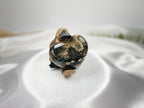 Treasured Energies large polished Ocean Jasper crystal heart held by a small wooden platypus figurine on white silk.